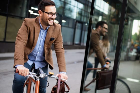 Feliz jovem elegante indo trabalhar de bike compartilhada